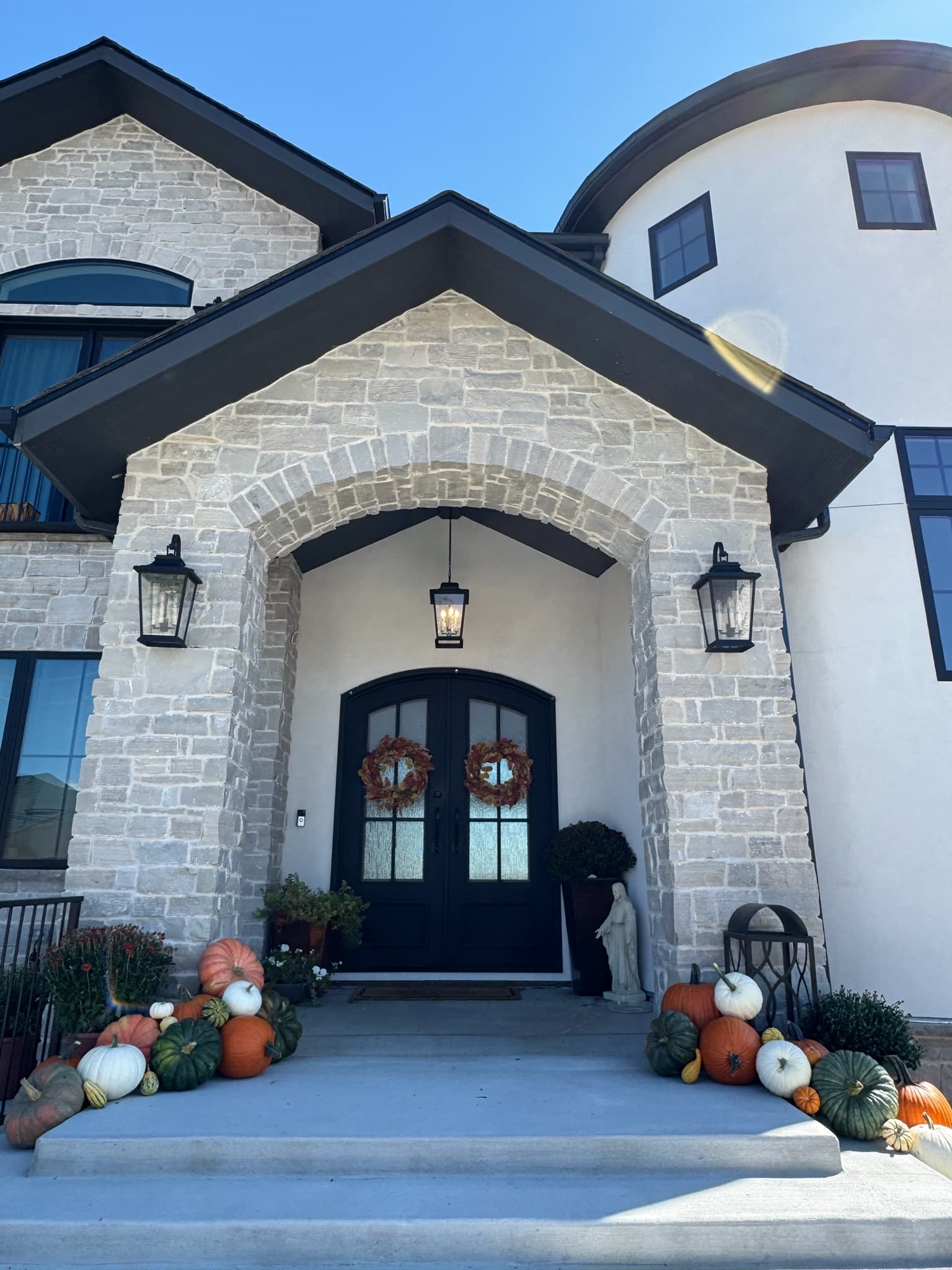 Gabled stone porch with dark double doors, autumn wreaths, and pumpkin clusters on the steps