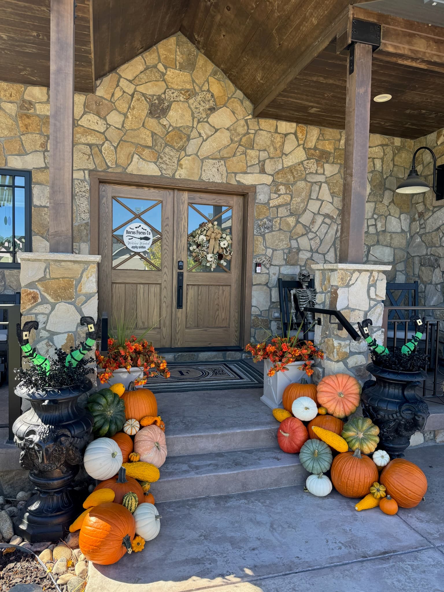 Wooden double doors with a fall wreath, Hocus Pocus sign, pumpkin piles, and a skeleton in a chair