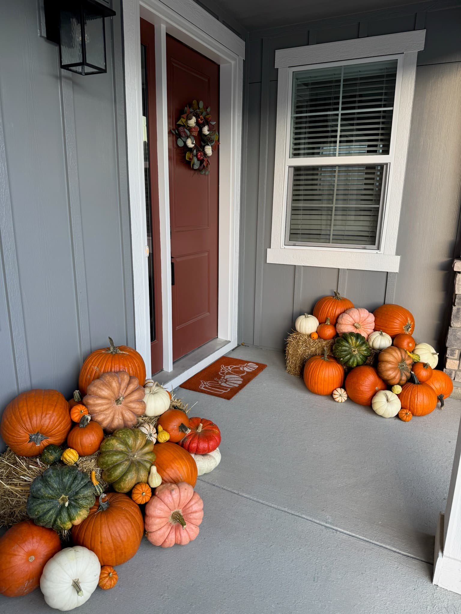 Burgundy door with a fall wreath, pumpkin doormat, and hay-bale pumpkin piles