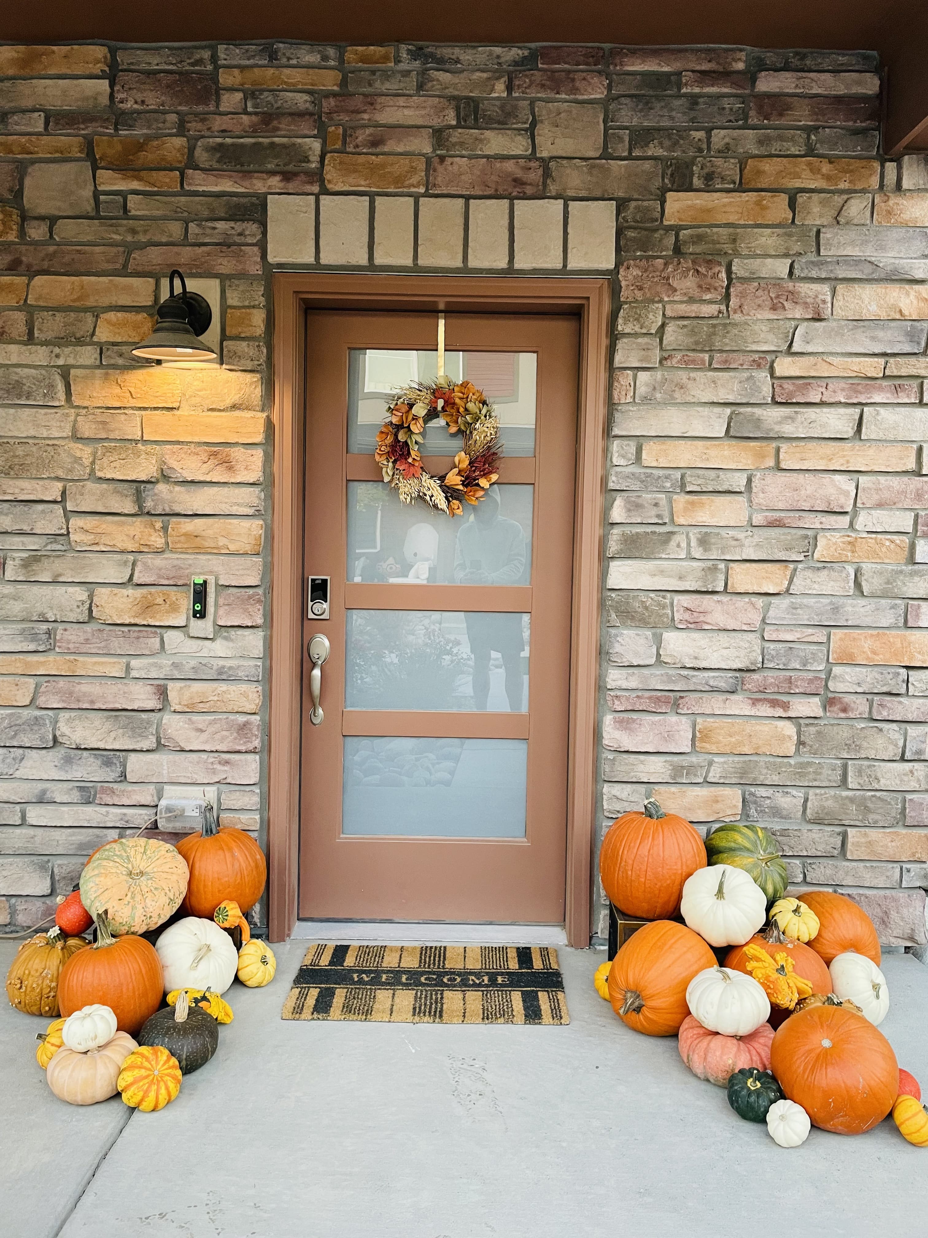Tan front door on a stacked-stone porch with a fall wreath and pumpkin clusters on both sides
