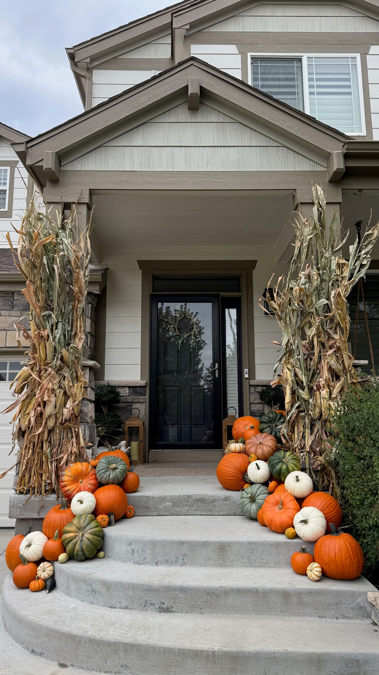 Straight-on view of a beige porch with corn stalks on the posts and pumpkins cascading down the steps
